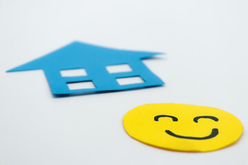 Yellow cut out paper smiley face with a blue paper house. on white background. concept of family...