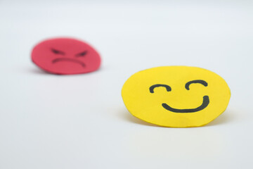 Yellow cut out paper smiley face with another red angry face in the background. on white...