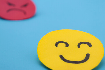 Yellow cut out paper smiley face with another red angry face in the background. concept of envy,...