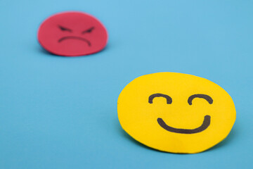 Yellow cut out paper smiley face with another red angry face in the background. concept of envy, selfishness, happiness or well-being - obrazy, fototapety, plakaty