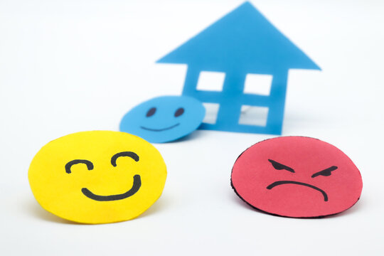Yellow cut out paper smiley face with another angry red face and a blue paper house. on white background. concept of problems at home, opinion of the real estate industry, buying and selling of house