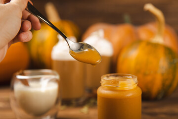 Organic pumpkin puree in a glass jar with fresh pumpkin, cinnamon and anise on a brown background....