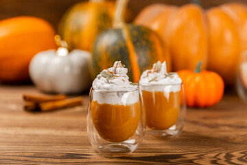 Pumpkin spice latte in glass mug with cinnamon, nutmeg, pumpkin seeds and whipped cream on brown...