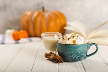 Pumpkin spice latte in blue mug with cinnamon, nutmeg, pumpkin seeds and whipped cream on white...