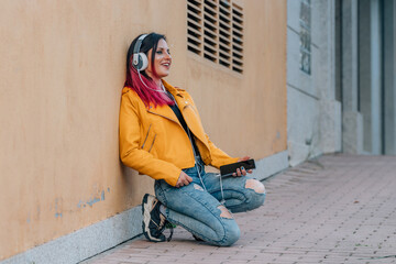 urban girl on the street sitting listening to music with headphones and mobile phone