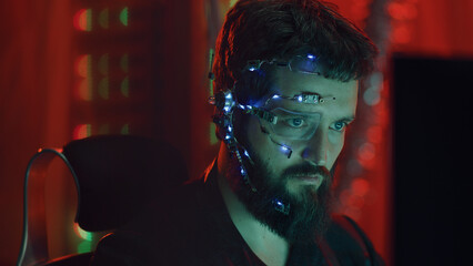 A Cyberpunk guy looks at the computer screen. Wearing futuristic one-eyed glasses with earpiece and...