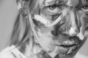 The girl's face is painted with paints on an isolated background, a black and white photo, a painting on the girl's face
