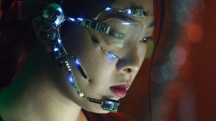 Focused asian girl in cyberpunk attire works on the computer. Wearing one-eyed glasses with white...