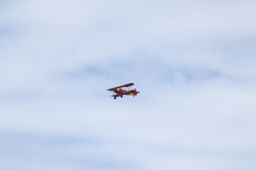 Fototapeta na wymiar Little red biplane flying across semi cloudy sky. This plane almost reminded me of the red baron. It has such an old look to it. I took this picture while standing on the beach in Cape May New Jersey.
