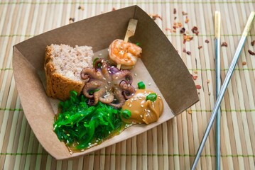 Paper plate with a portion of seafood, shrimp, octopus, Chuka seaweed, nut sauce, slice of bread. Street food.