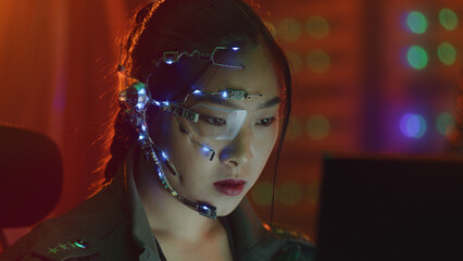 Focused asian girl in cyberpunk attire works on the computer. Wearing one-eyed glasses with white...