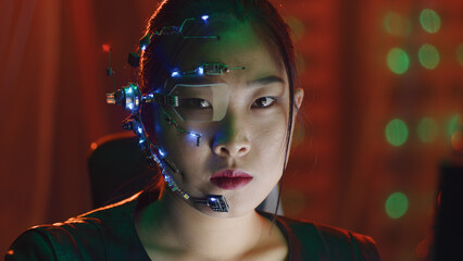 Asian girl in cyberpunk style wearing one-eyed glasses and microphone with small LED lights looks...