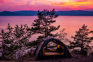 Tent on a hill near the lake against the backdrop of a picturesque sunset