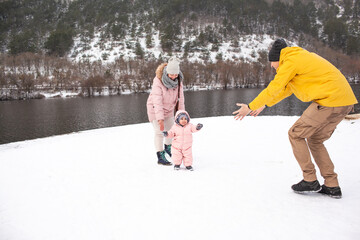 Happy family have fun with one-year-old baby in the snow, people dresed warm clothes iand walking in the winter vacations