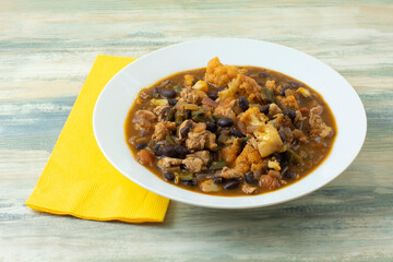 Chicken cauliflower and bean stew in white soup bowl with yellow napkin