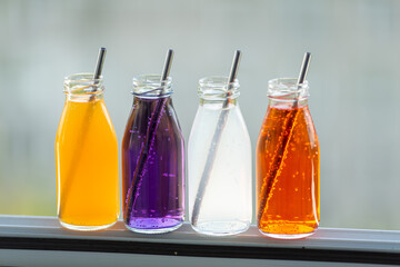 Colored bottled drinks on a blurry background, open space, white, light blue, yellow, orange. purple, alcohol, not alcohol