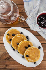 Pancakes with berries (black currant) with tea and a jam dish for a tasty morning breakfast on a wooden background. Copy space text, concept for the menu, a stylish serving of the dish