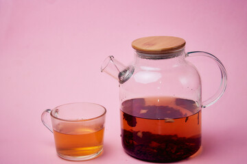 tea in a transparent glass teapot and in a glass cup on a pink background