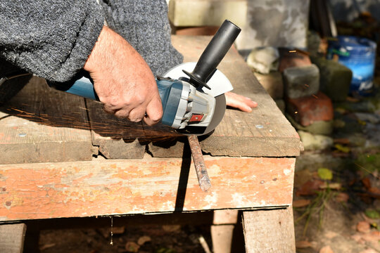 In the picture, a worker with a grinder on a workbench cuts off a piece from a metal rod.