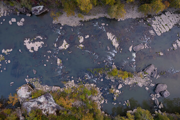 An aerial drone image of the New River in West Virginia. The water is flowing. Nobody is in the image. The surrounding forest is changing to autumn colors. 