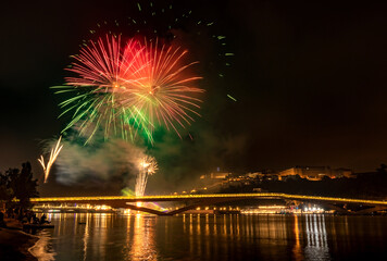 Fototapeta premium Nightly fireworks at the festivities in the city of Coimbra 2022, in Portugal, with the Mondego River and the Pedro e Inês pedestrian bridge in the foreground and the university in the background.