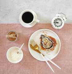 Cinnamon bun with cream on a plate with cup of coffee and alarm. Breakfast concept, top view