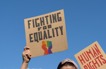 People holding placard signs slogans Fighting for Equality, with rainbow flag fist and Human...