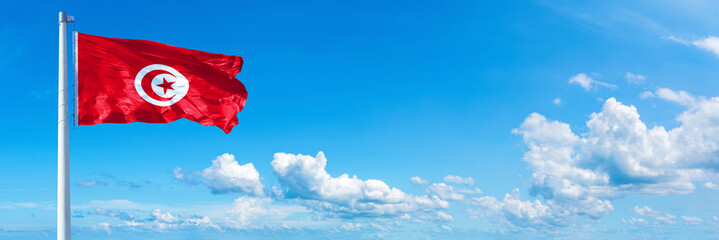 Tunisia flag waving on a blue sky in beautiful clouds - Horizontal banner