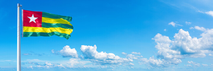 Togo flag waving on a blue sky in beautiful clouds - Horizontal banner