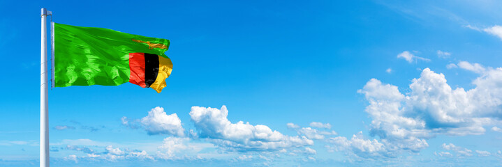 Zambia flag waving on a blue sky in beautiful clouds - Horizontal banner
