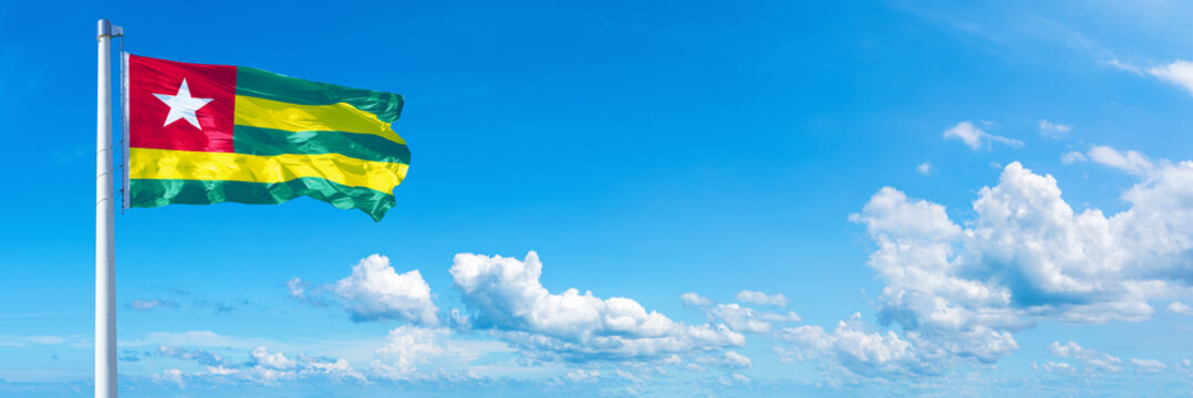 Togo flag waving on a blue sky in beautiful clouds - Horizontal banner