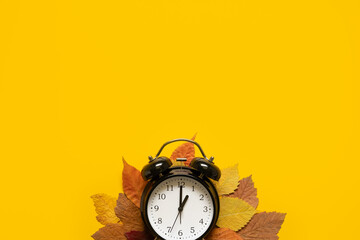 Autumn composition sale banner with dried leaves and black alarm clock on pastel yellow background....
