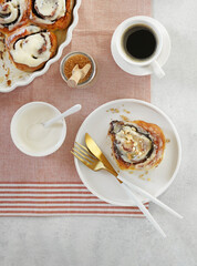 Cinnamon bun with cream on a plate with cup of coffee and cream. Breakfast concept, top view, vertical orientation