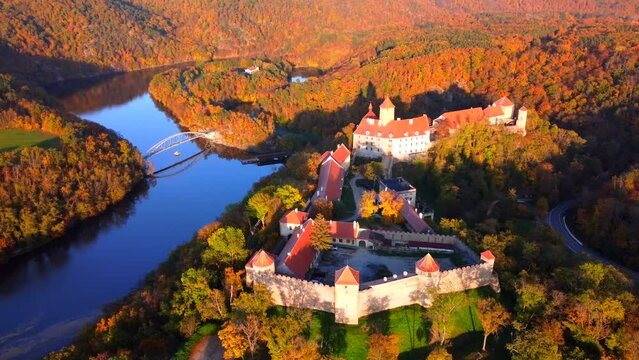Flying over ancient castle in big circles, aerial view on beautiful autumn colored countryside with river in the background.