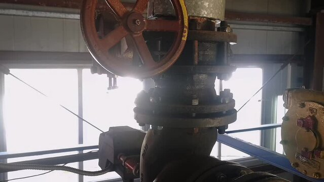 An old valve with a yellow round steering wheel on a heating pipe in a boiler room.
