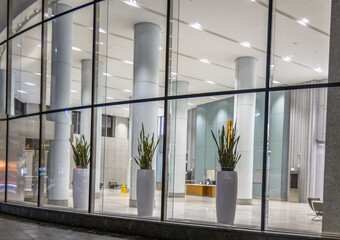 Typical empty commercial building lobby at night, large curved window, pillars and planters in...