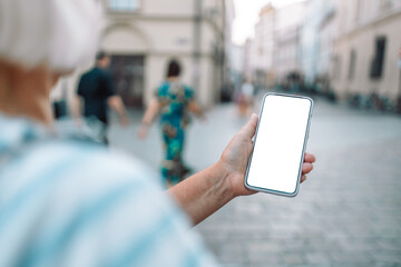 Young woman holding cellphone with blank white screen in urban city surroundings. 