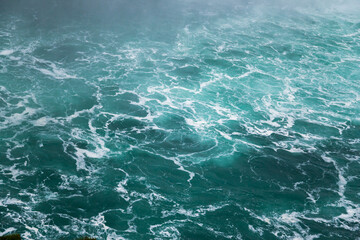 Fototapeta na wymiar Defocused water background - whirlpool waves, blue tint. Abstract background with liquid fluid texture. Niagara river 