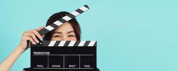Asian Woman holding black clapperboard and closing her face on mint green background.