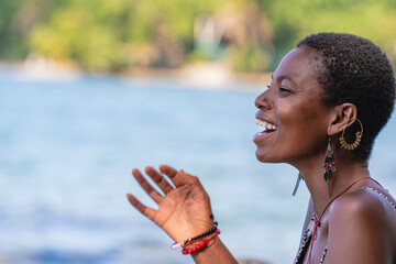 Retrato horizontal de una mujer africana de cabello afro corto, muy sonriente y feliz en una playa...