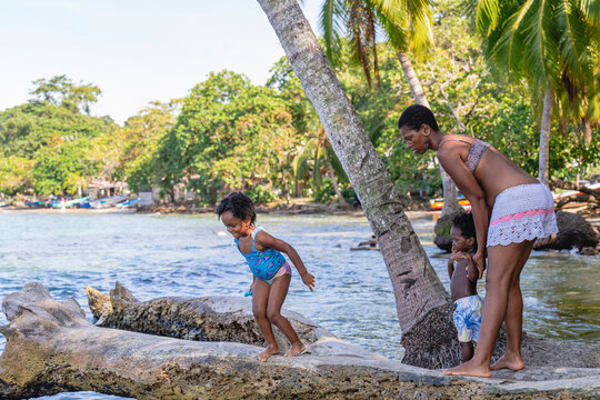 imagen de una hermosa familia en la playa del caribe en Costa Rica jugando sobre un tronco de madera saltando al agua