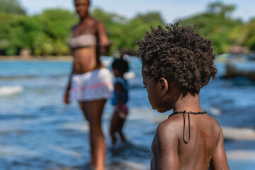 Imagen horizontal de un pequeño niño afroamericano con cabello afro de espalda en la playa en un...