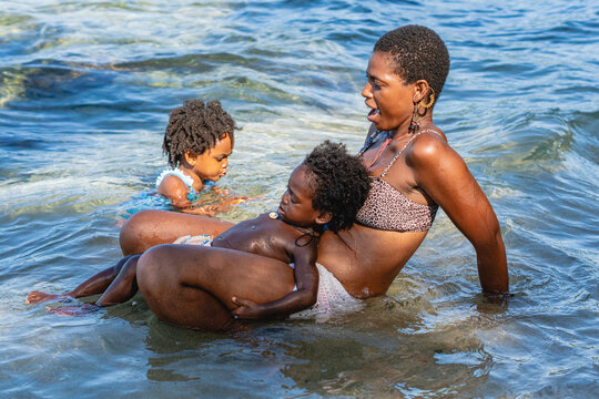 Imagen horizontal de una madre y sus pequeños hijos afroamericanos jugando juntos a la orilla del mar en un hermoso día de verano.