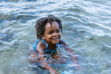 Imagen horizontal de una hermosa niña afroamericana de cabello afro muy sonriente sola jugando en...