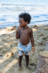 Imagen vertical de un pequeño niño afroamericano de cabello afro de pie solo en la playa con su...