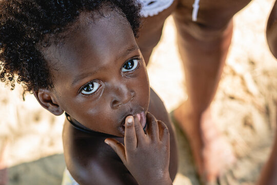 Imagen cenital del rostro de un peque&ntilde;o ni&ntilde;o afroamericano con cabello afro en exterior mirando hacia arriba mientras mete su dedo en su boca.  