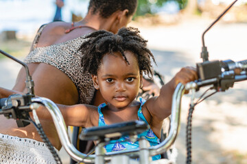 Obraz premium Imagen horizontal de una pequeña niña afroamericana mirando a cámara mientras se sostiene del manubrio de una motocicleta. 