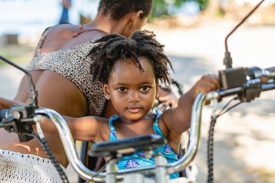 Imagen horizontal de una pequeña niña afroamericana mirando a cámara mientras se sostiene del manubrio de una motocicleta. 
