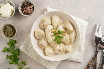 traditional ukrainian east european dish varenyky or chinese wan tan or dim sum - dumplings stuffed with minced meat, fresh cilantro, herbs in white bowl on beige colored kitchen towel. Top view