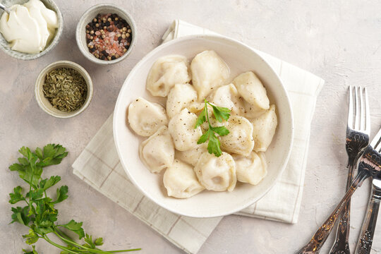 traditional ukrainian east european dish varenyky or chinese wan tan or dim sum - dumplings stuffed with minced meat, fresh cilantro, herbs in white bowl on beige colored kitchen towel. Top view